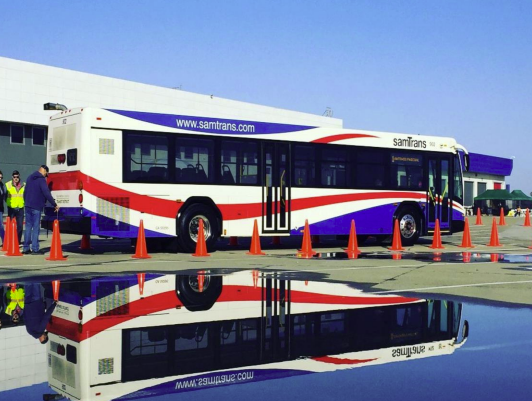 Child riding in a replica SamTrans bus next to a real SamTrans bus